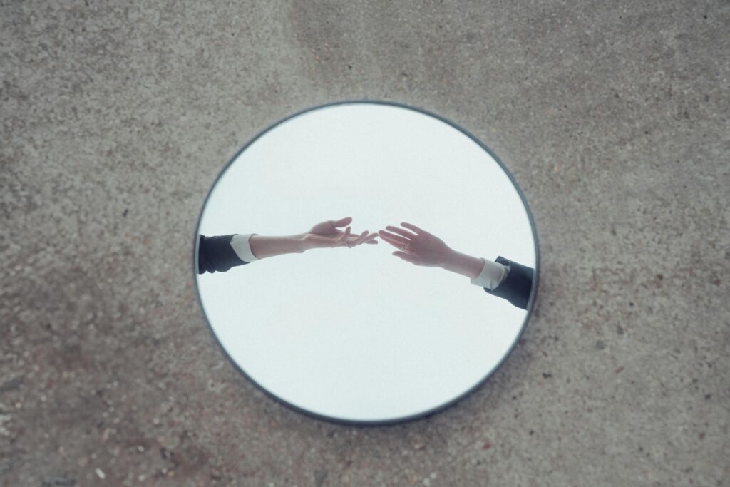 pexels-photo-20616956-20616956 Conceptual image of hands reaching out, reflected in a round mirror on textured ground.